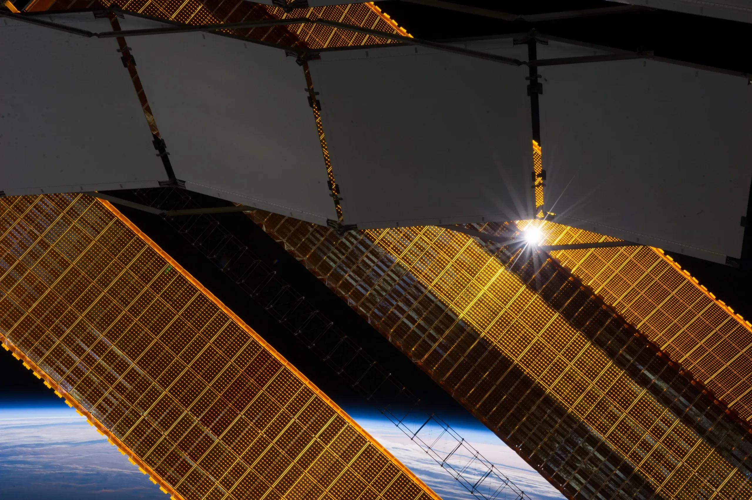 Photograph of white radiator panels and gold solar arrays on the International Space Station, with the Earth below