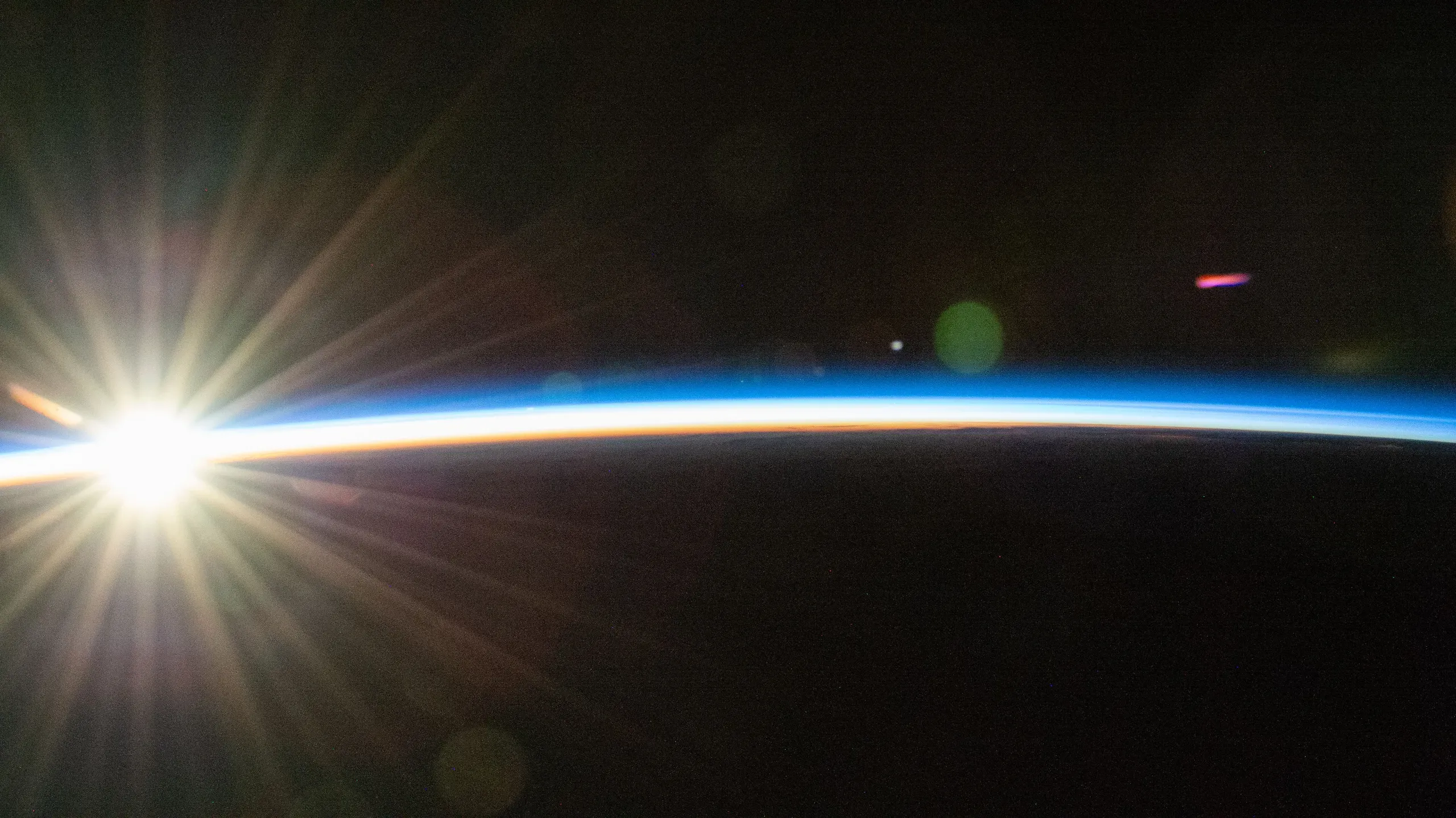 Photograph from orbit: the sun rising over the dark curve of the Earth, lighting the thin blue line of the atmosphere